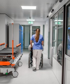 A photo of a nurse pushing a patient in a wheelchair in a hospital corridor.