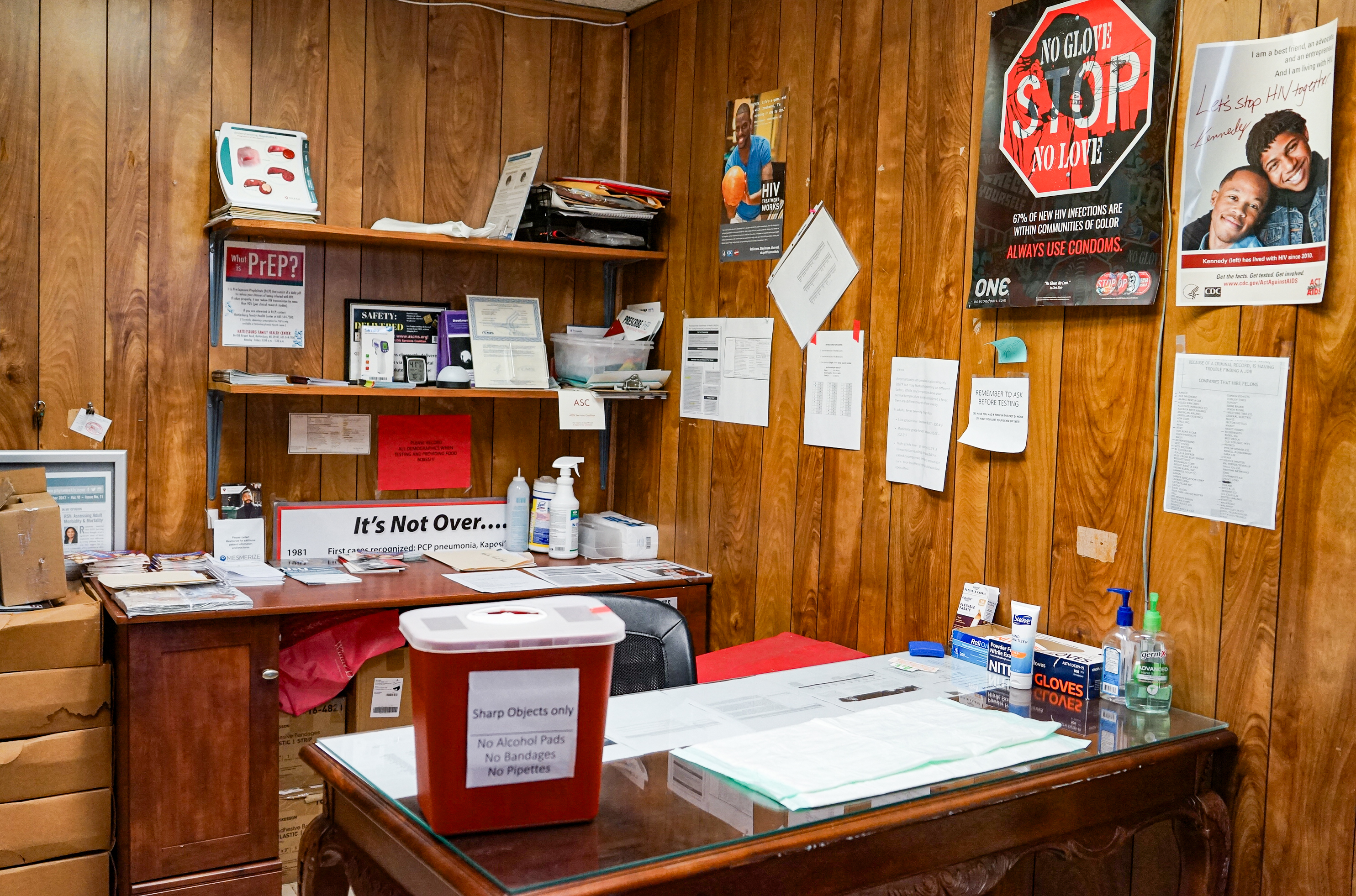 An empty office room that once functioned as an HIV clinic. There are papers and posters on the wooden walls with information about HIV.