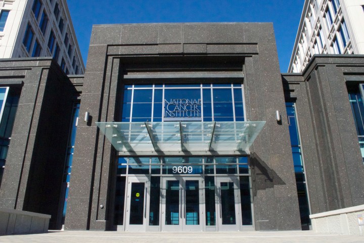 A photo of the front of a research building. A sign on the front reads, "National Cancer Institute."