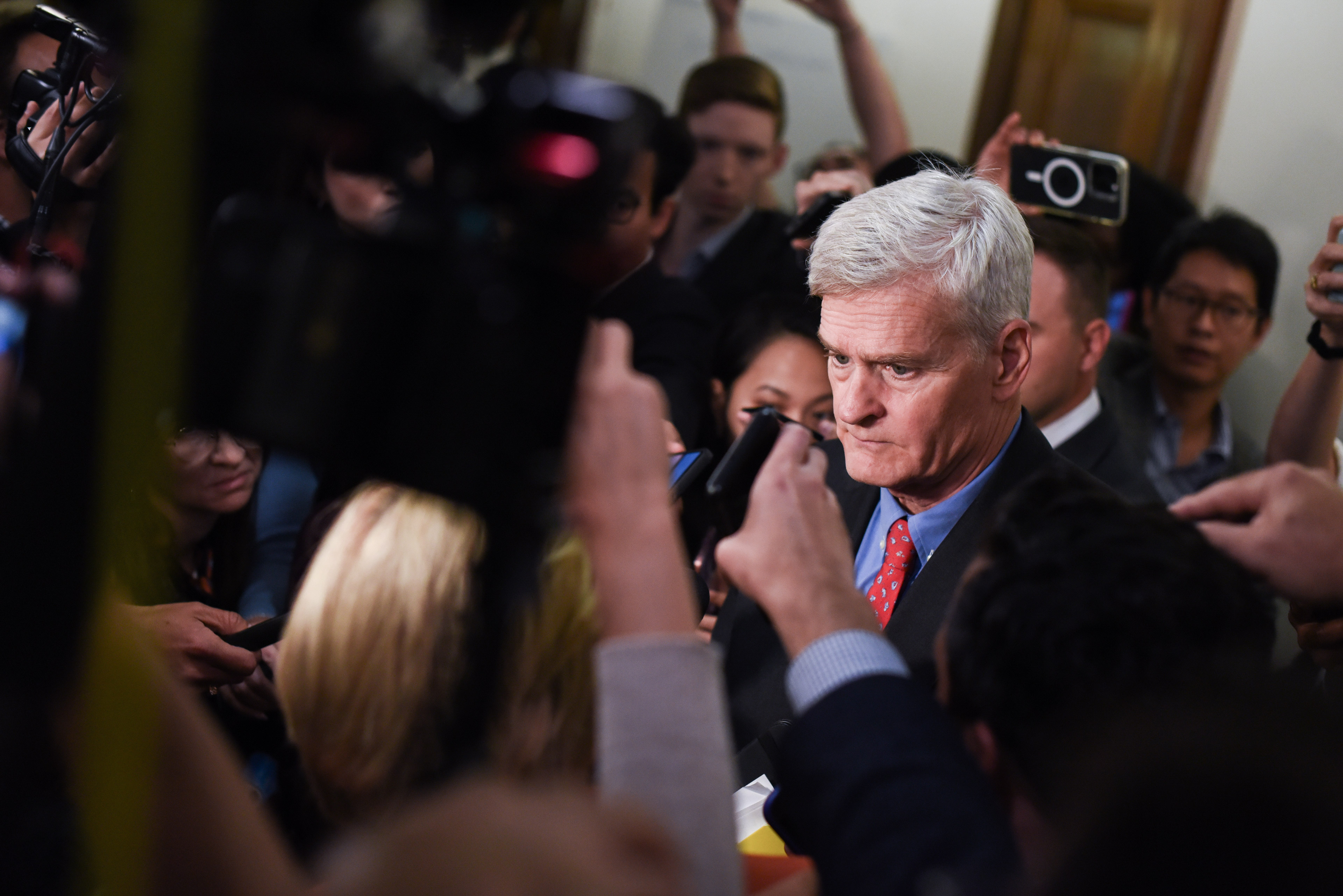 Een groepje verslaggevers met hun telefoons en videocamera's in de lucht interviewt senator Bill Cassidy in een gang van de Senaat.