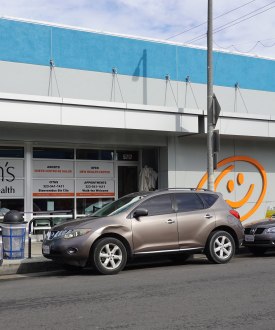 A photo of a health clinic's exterior. Cars are parked on the street in front of it.
