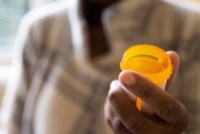 A photo of a hand holding an opened pill bottle.