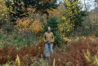A photo of a woman standing in a meadow in autumn. The foliage around her is turning orange and yellow.