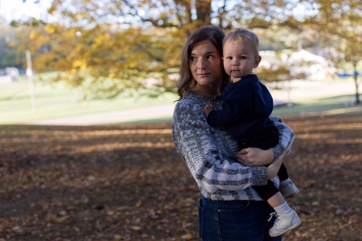 A photo of a woman holding her toddler outside.