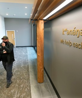 Two men walk beside each other in the hallway of a health clinic. Signage on the wall reads, "we help each other."