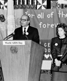 A black and white photograph from 1988 shows Rafeeuddin Ahmed, Chairman of the UN Steering Committee for the Prevention and Control of AIDS, speaking at the opening ceremony. On the right is Mrs. M Perez de Cuellar, wife of the UN Secretary-General.