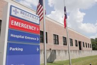 A photo of an emergency room sign for Bellville Medical Center. The American flag and the Texas flag are seen on poles next to it.