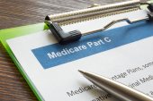 A green clipboard with a Medicare Part C form. A pen rests on top of the form.