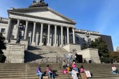 A small group of people sit and stand on the steps of the South Carolina State House.