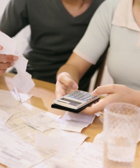 A man and woman seated at a table with papers, bills, receipts, and a calculator in front of them