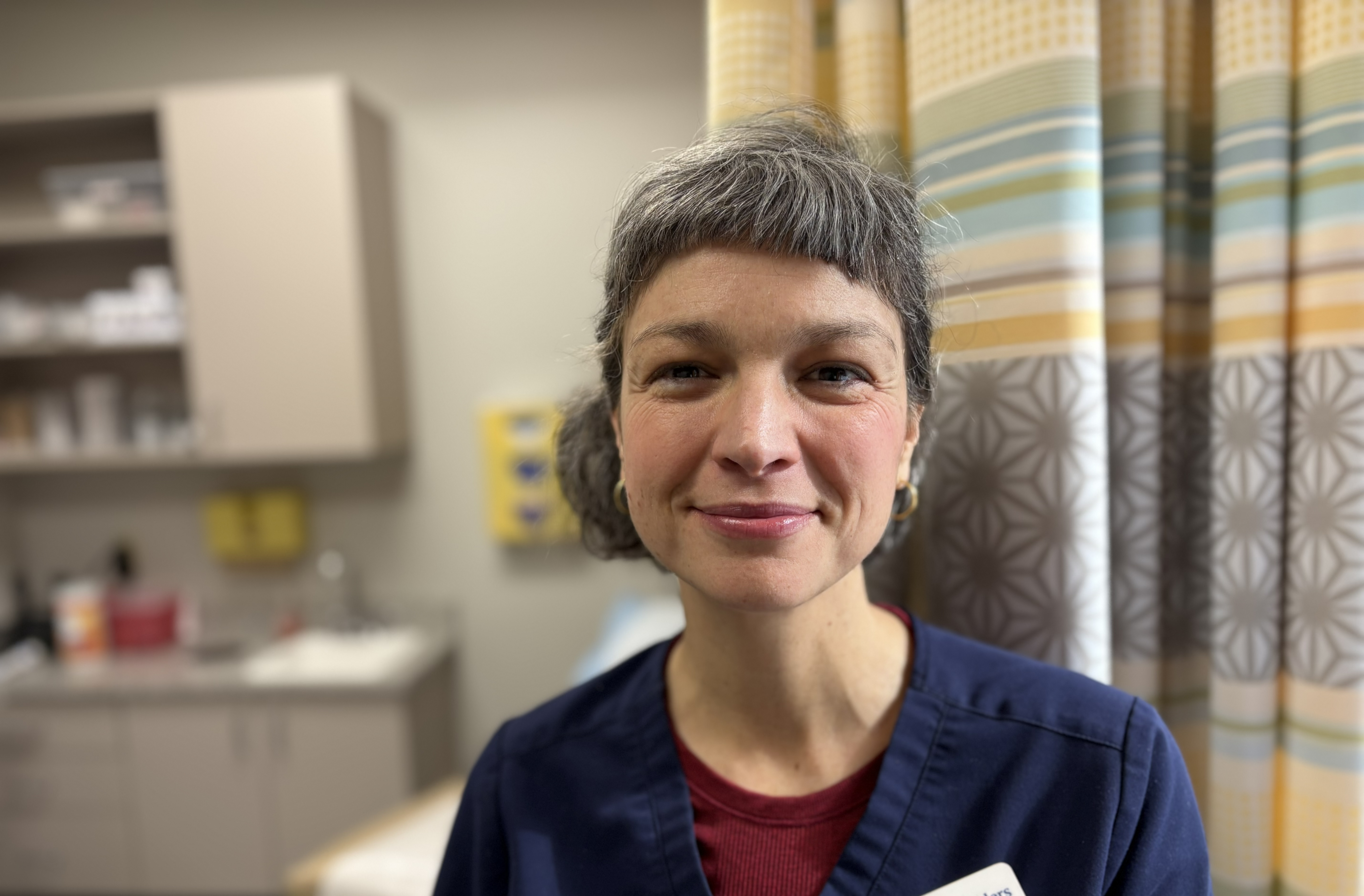 A close up of a woman with bangs in navy scrubs.