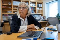 A researcher sits at her desk indoors. A laptop is in front of her.