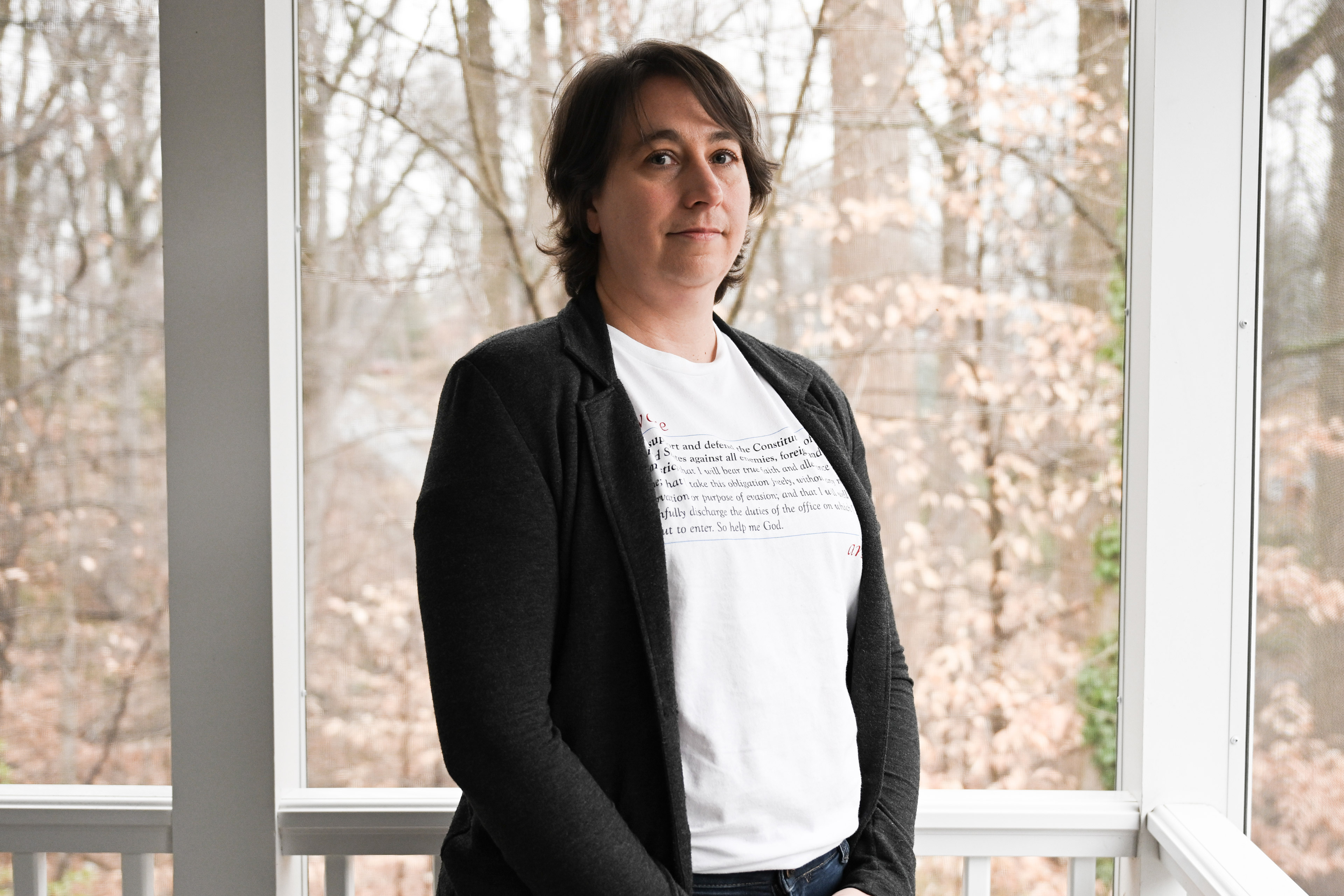 Alexa Romberg stands in a screened-in porch area in her home. She wears a shirt with her oath of office written on it.