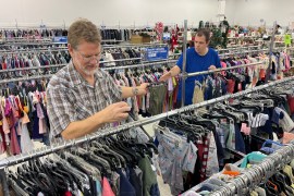 Two men sort racks of clothes in a Goodwill store.