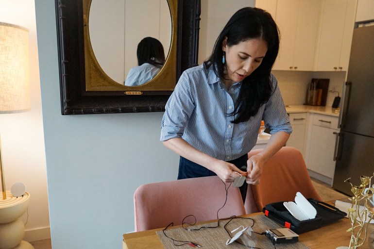 A woman leans over a dining room table, where she handles a medical device.