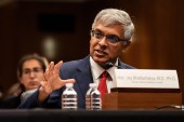 Jay Bhattacharya speaks while sitting at a table with his nameplate, and two water bottles, in front of him.