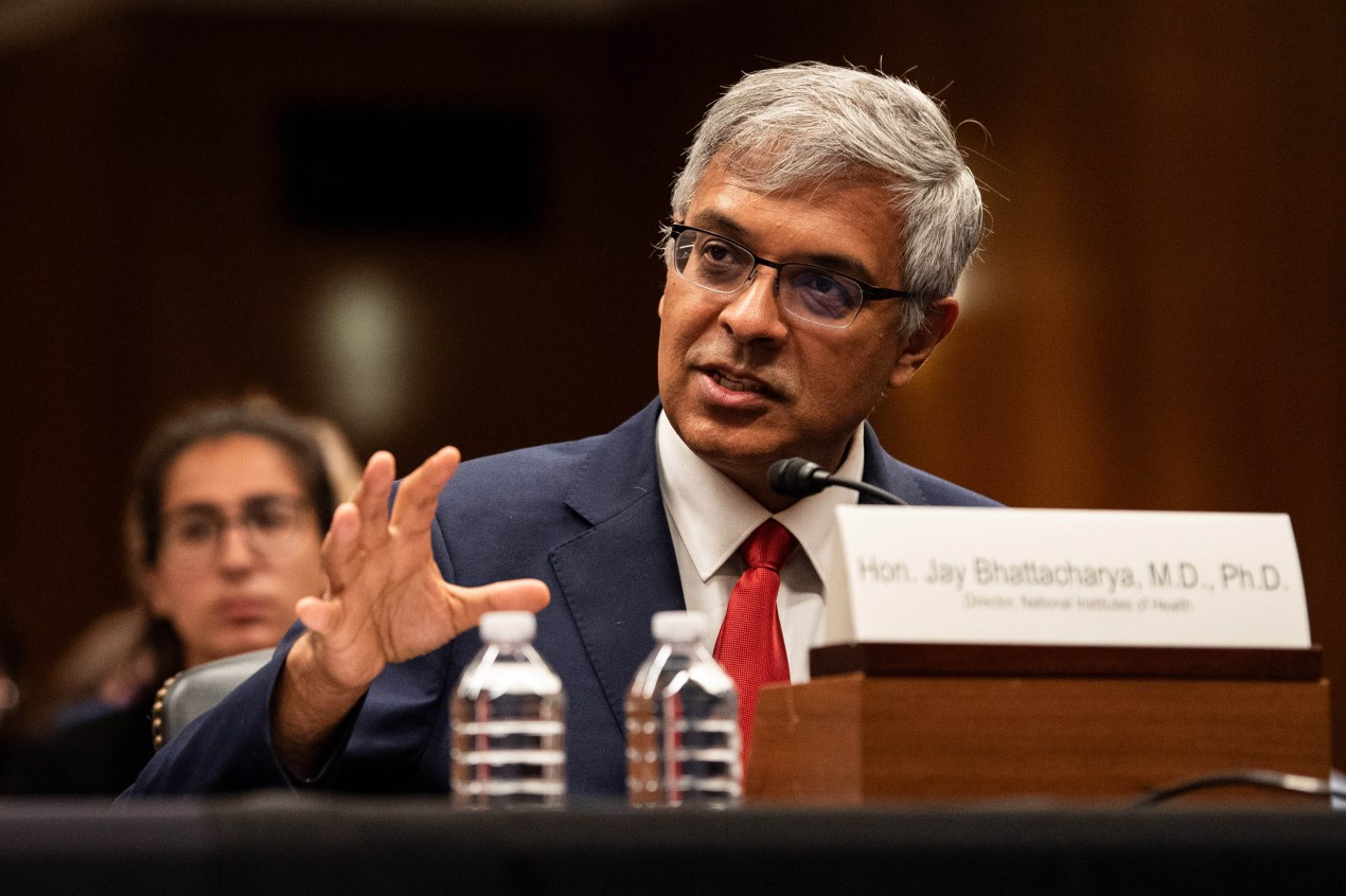 Jay Bhattacharya speaks while sitting at a table with his nameplate, and two water bottles, in front of him.