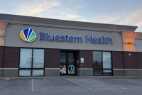 An exterior of a health clinic with a blue sign that reads, "Bluestem Health."