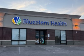 An exterior of a health clinic with a blue sign that reads, "Bluestem Health."