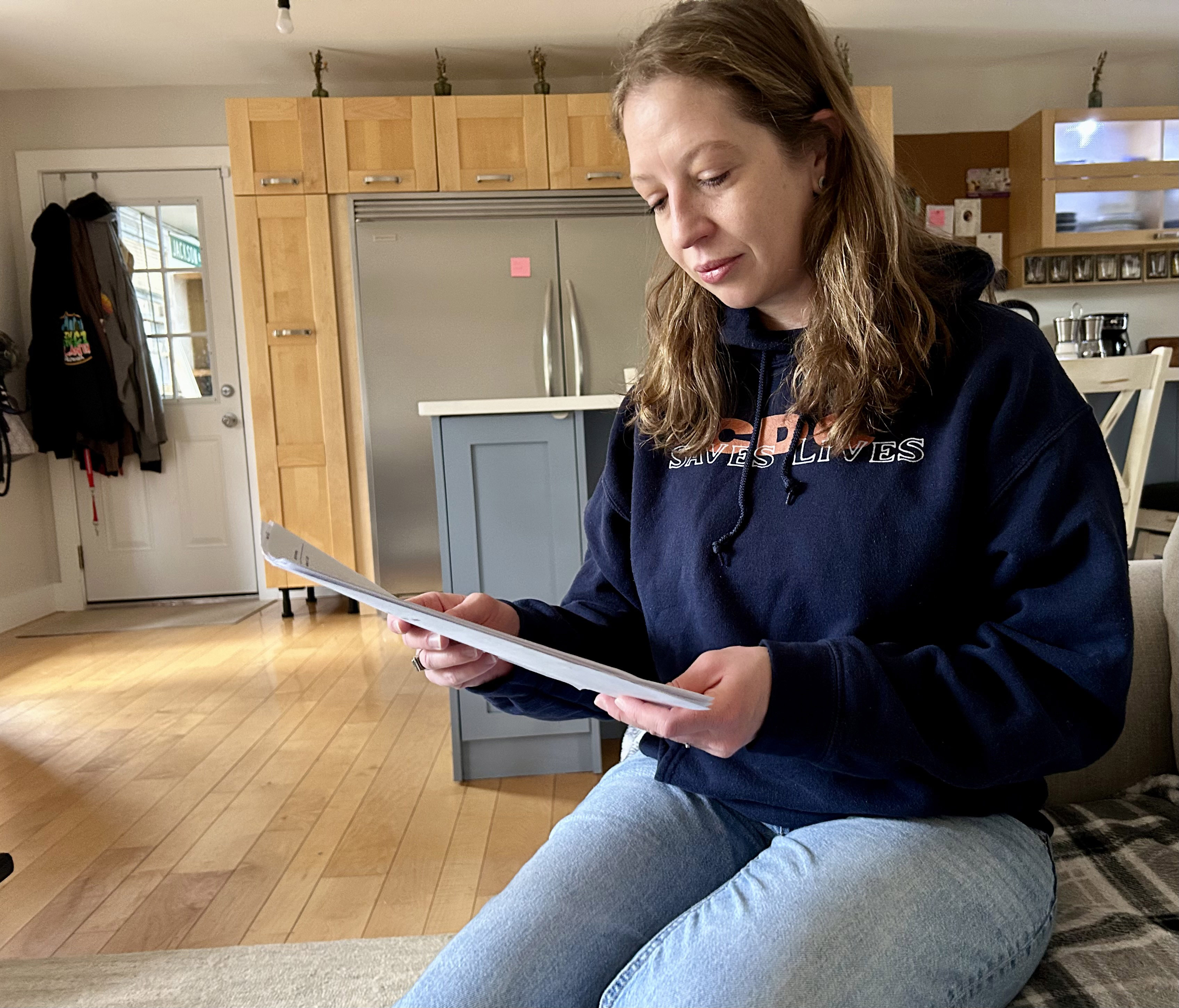 A woman sits on a couch holding papers that she's reading
