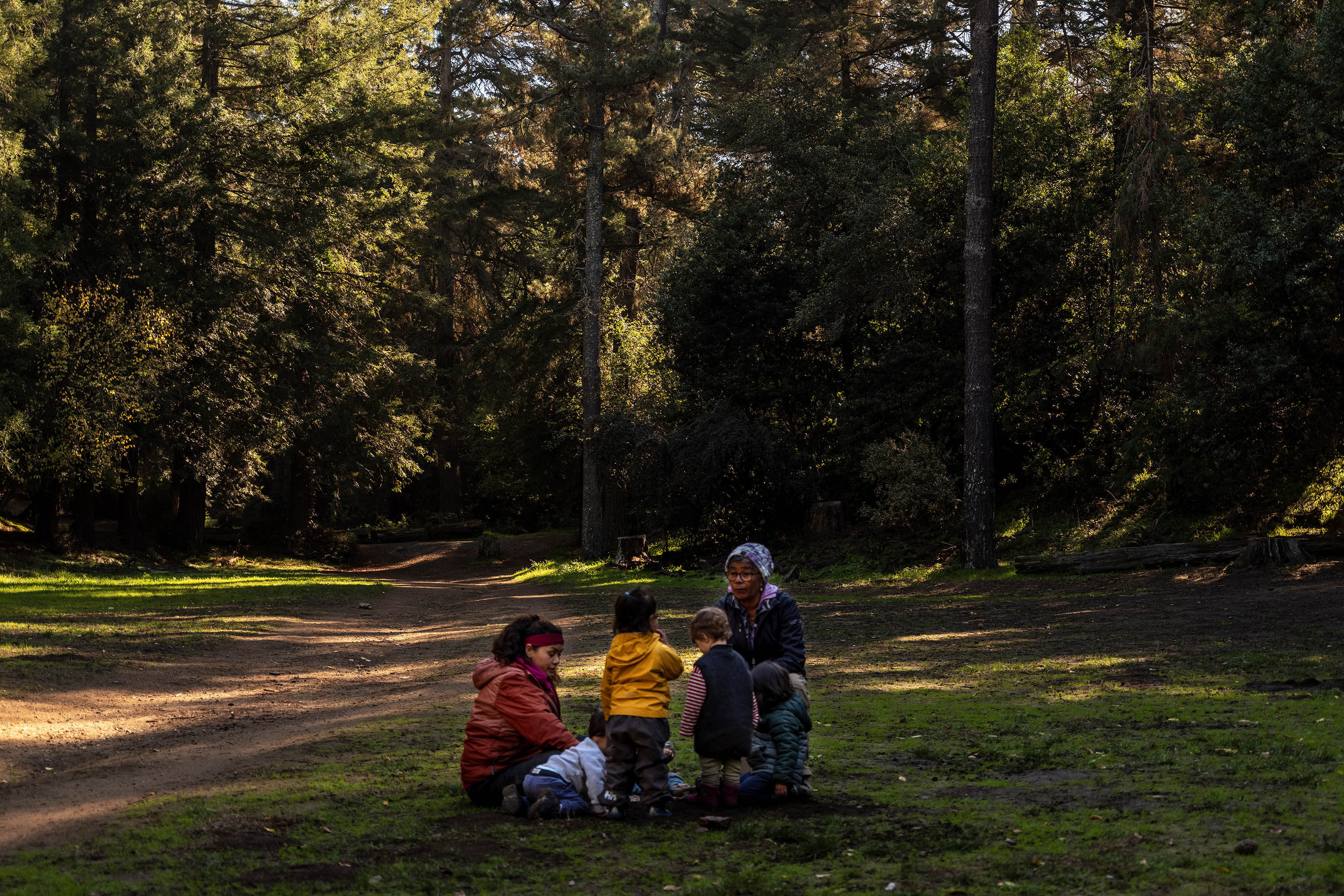 Two adult women gather a small group of toddlers before a walk through a redwood forest nature trail.