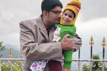 A father holds his young daughter outside.