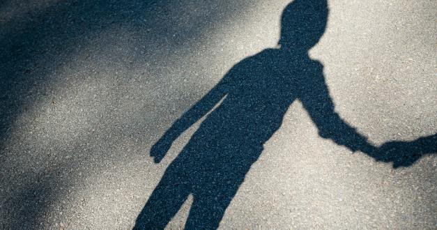 A shadow of a young boy is cast against the pavement. The boy is holding an adult's hand out of frame.