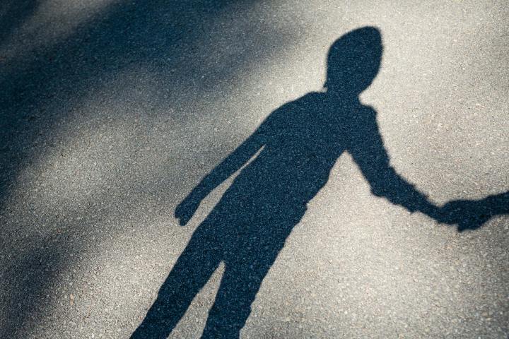 A shadow of a young boy is cast against the pavement. The boy is holding an adult's hand out of frame.