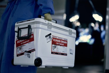 A medical worker carries an ice box with a label on it that reads, "Human organ for transplant."