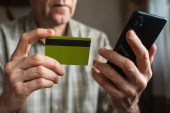 A senior man looks at a credit card while on his phone