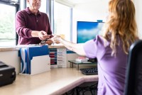 A man at a doctor's office hands over a credit card to a receptionist at the front desk.