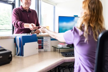 A man at a doctor's office hands over a credit card to a receptionist at the front desk.