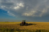 A tractor is parked in a field. Dark clouds are moving overhead.