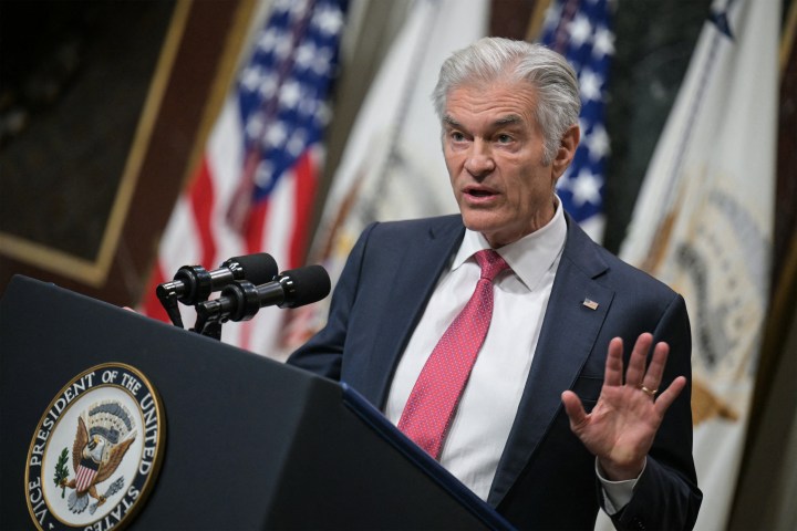 A photo of Mehmet Oz speaking at a podium at the White House. American flags are seen behind him.