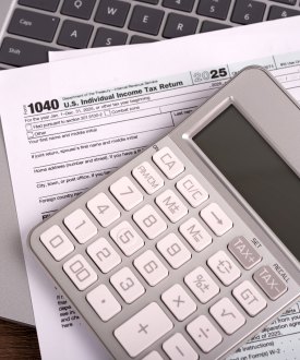 A set of tax forms and a calculator rest on top of a laptop.