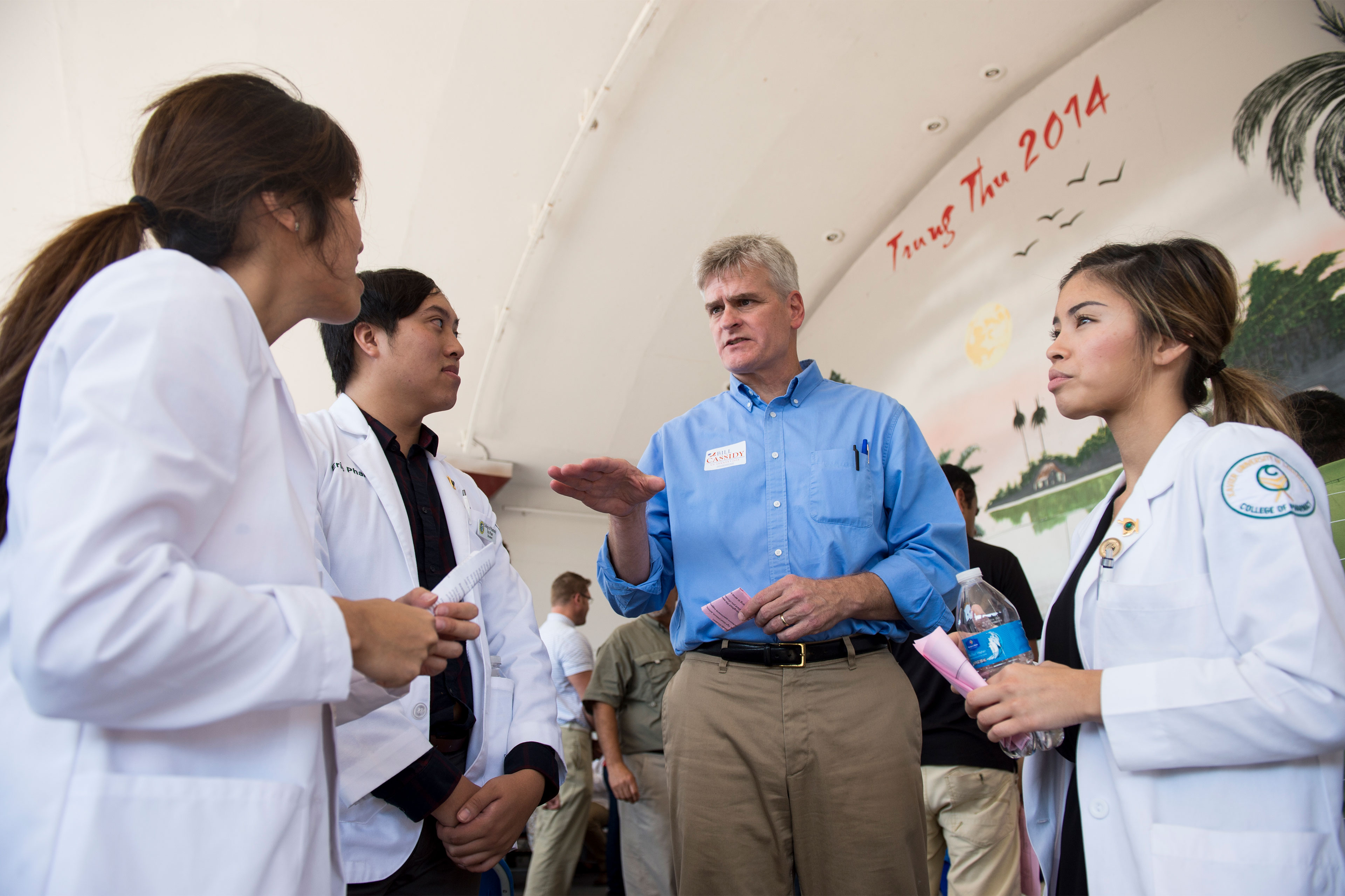 Bill Cassidy stands in the center of the frame. He's surrounded by three medical students in white coats.