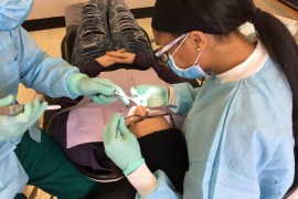 A photo from above of a person lying in a dental chair having work done. A dentist and assistant sit on either side of the patient's head.