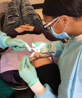 A photo from above of a person lying in a dental chair having work done. A dentist and assistant sit on either side of the patient's head.