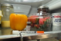 A syringe rests on the top shelf of a fridge.