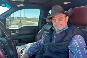 An older man wearing a brown cowboy hat sits in the driver's seat of a truck.