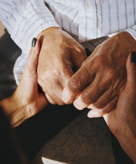 A woman holds the hands of a senior man.
