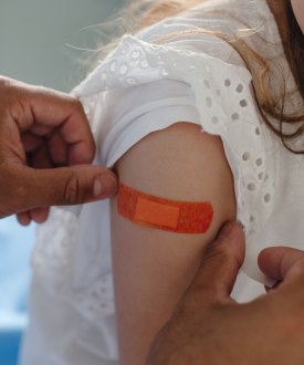 A doctor applies a bandage to a young girl's arm after she receives a vaccine.