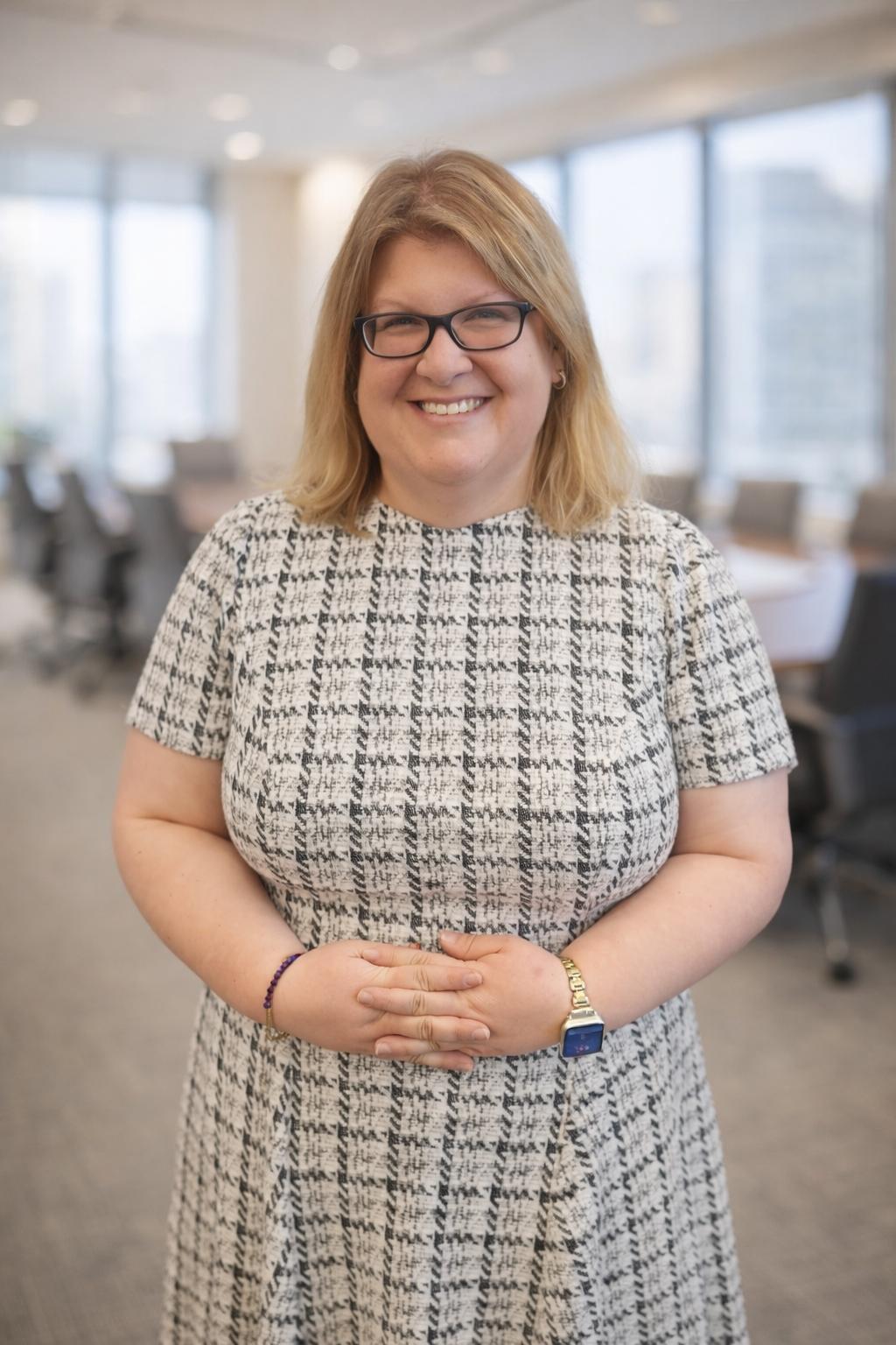 A woman stands inside at an office. She is smiling.