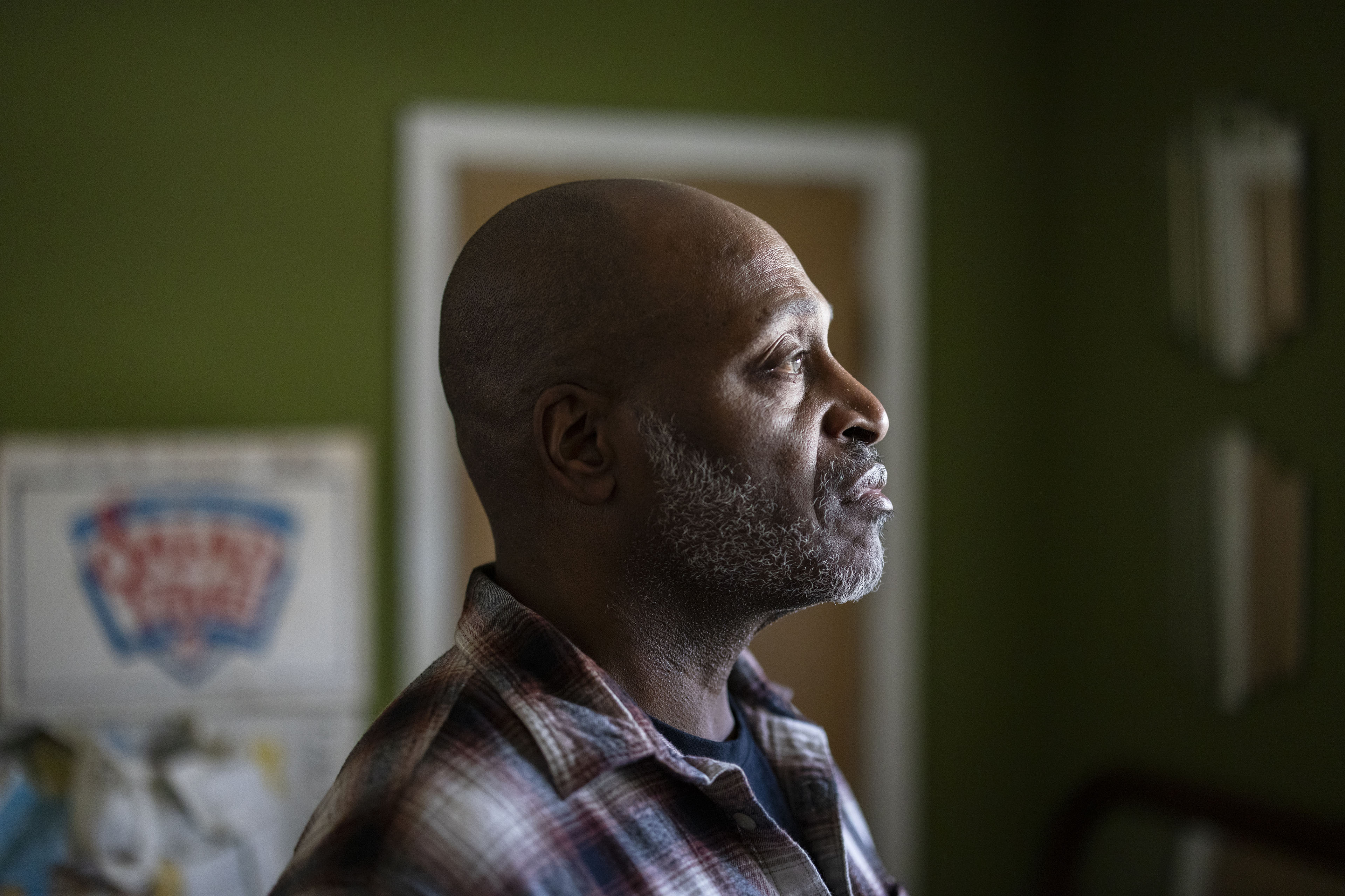 A photograph of the profile of a man, facing sunlight through a window, as he stands in a room with green painted walls