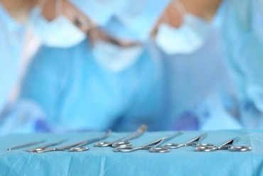Surgical tools lying on table while group of surgeons at background operating patient in surgical theatre. Steel medical instruments ready to be used. Surgery and emergency concept