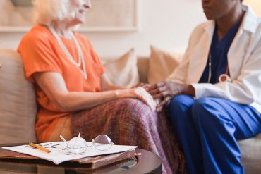 Senior woman holding hands with doctor in home