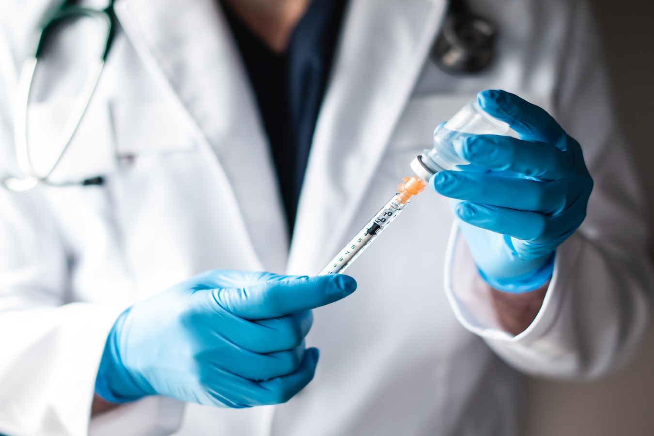 Doctor in white coat drawing vaccine into a syringe for injection.