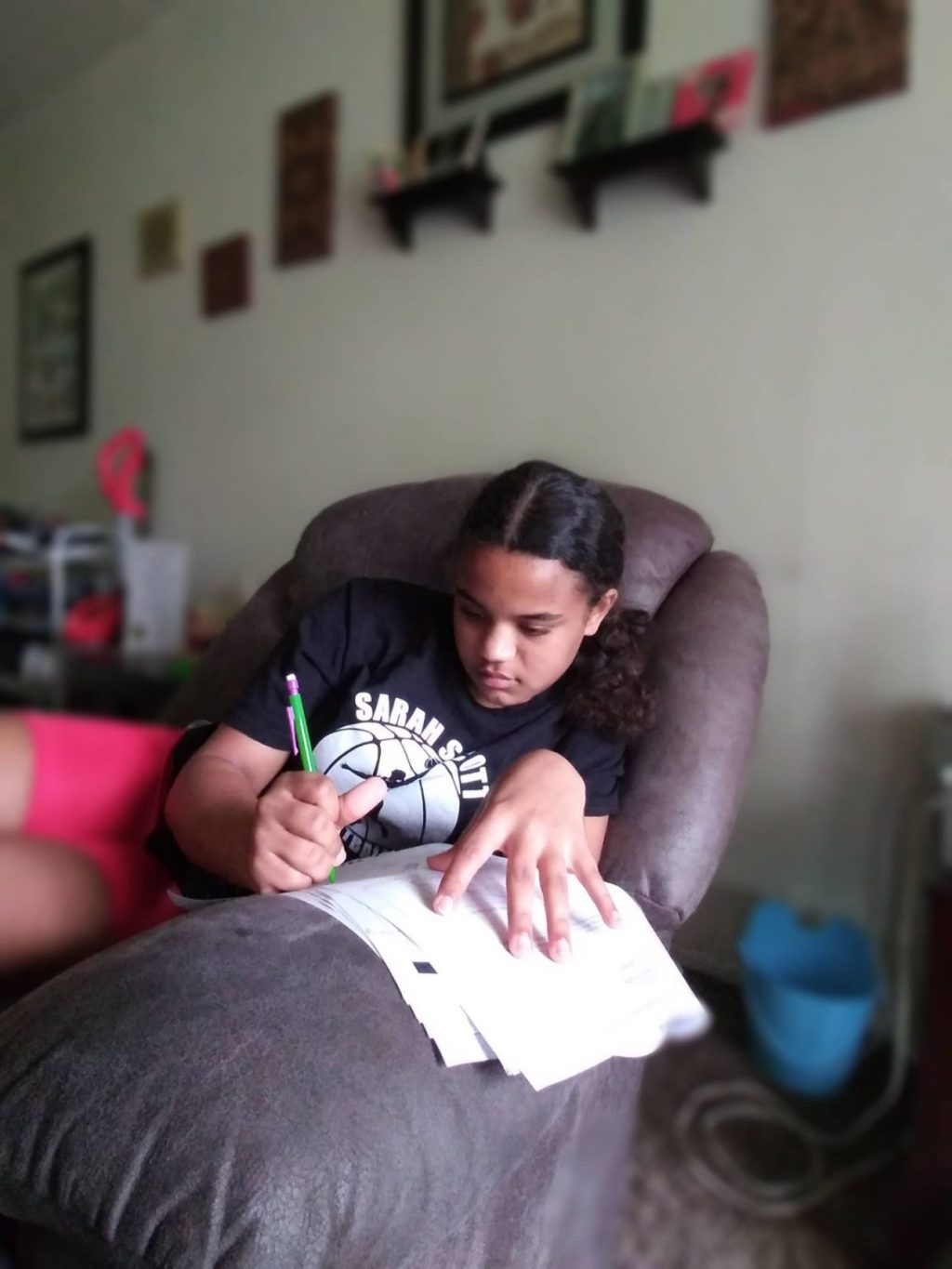 young girl writing while seated on couch with papers on the armrest and a pen in hand
