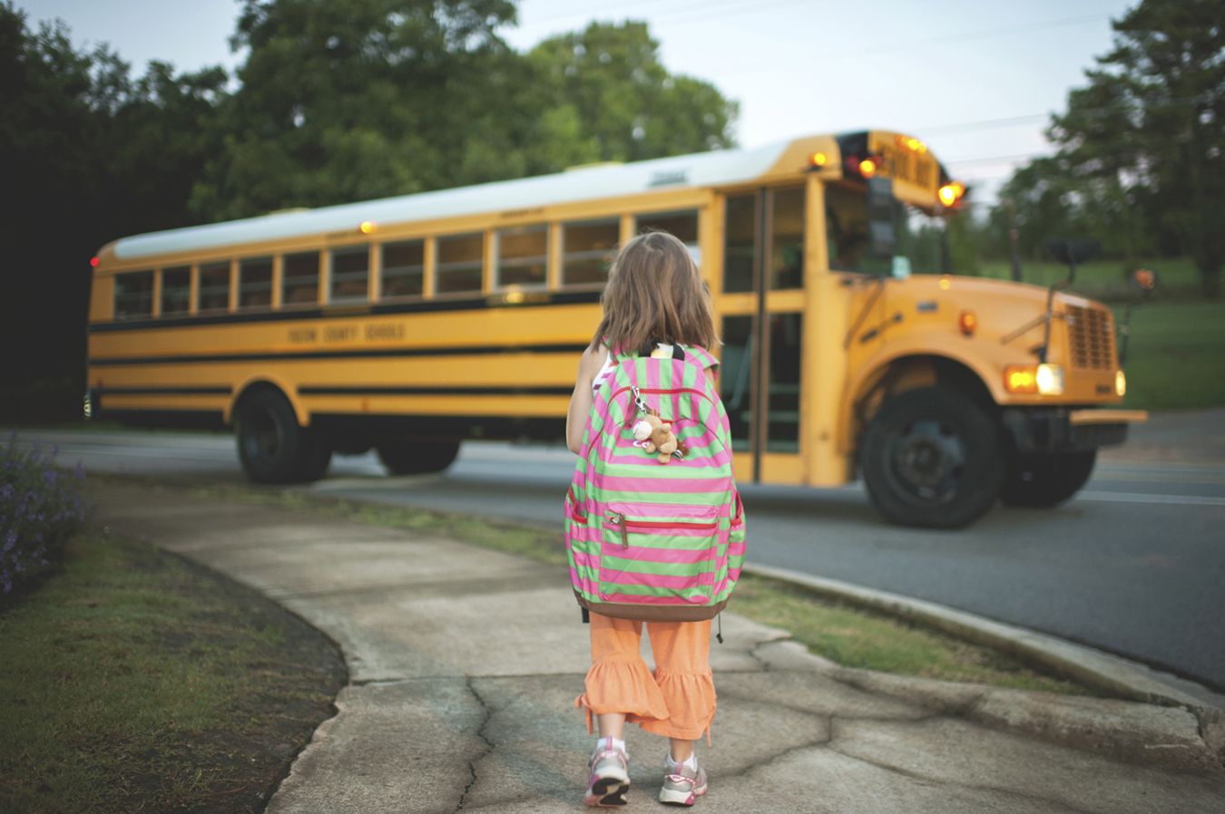 Rear view of schoolgirl with backpack waiting for bus while standing on footpath