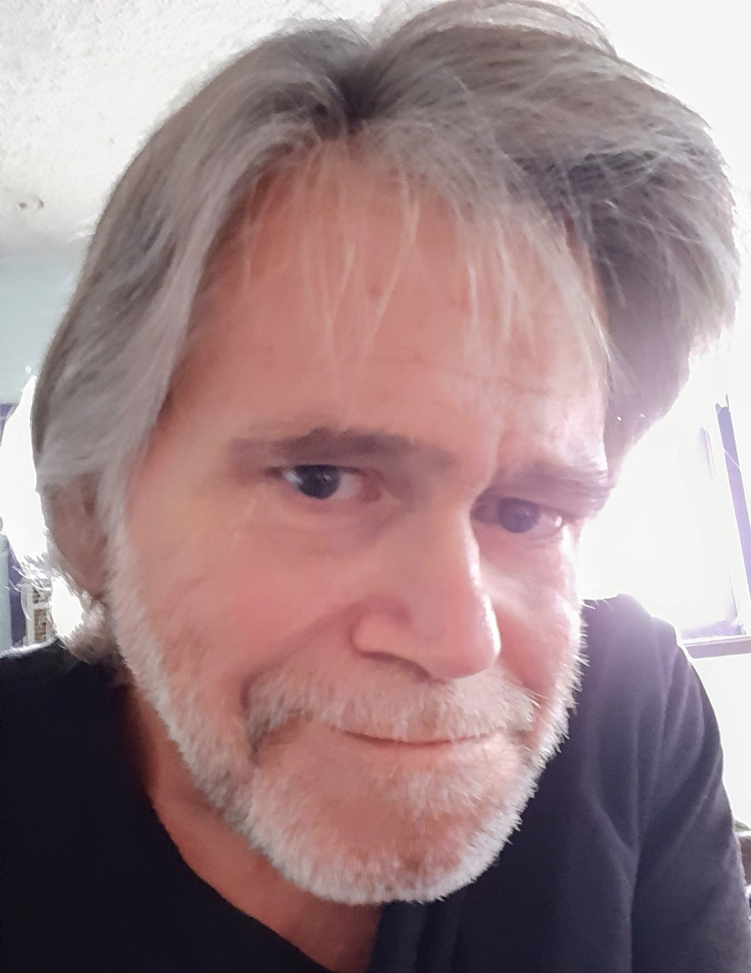 Fred Axelrod, a Los Angeles 66-year-old, looks at the camera. He has a gray wispy hair that falls over his face slightly.